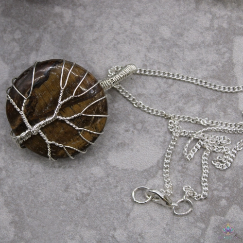 Collier Arbre de Vie Œil de Tigre 3 Collier arbre de vie en œil de tigre posé près d'une roche minérale, chaîne gourmette déroulée