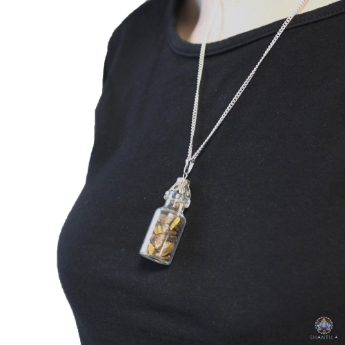 Collier Fiole d'Éclats d'Œil de Tigre 3 Collier fiole d'éclats d'œil de tigre porté sur un haut noir, le pendentif tombant sous les clavicules, vue de trois quart