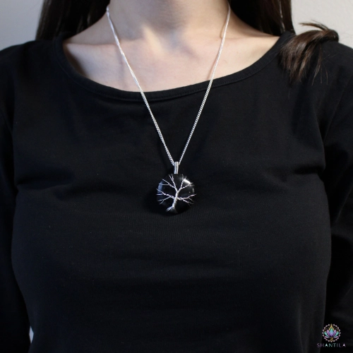 Collier Arbre de Vie Onyx Noir 2 Collier arbre de vie en onyx noir porté sur un haut noir, le pendentif tombant sous les clavicules
