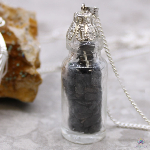 Collier Fiole d'Éclats d'Onyx Noir 3 Collier fiole d'éclats d'onyx noir posé près d'une roche minérale, chaîne gourmette déroulée