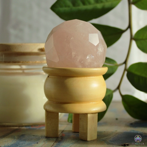 Sphère Quartz Rose Facettée et son Pied en Bois — 5 cm 4 Sphère en quartz rose facettée sur son pied en bois, devant des feuillages et une bougie