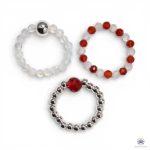 Trio de bagues élastiques en pierres naturelles — pierre de lune laiteuse et rubis rouge profond — présentées sur fond neutre avec perles argentées, dans une palette de blanc nacré et rouge intense.