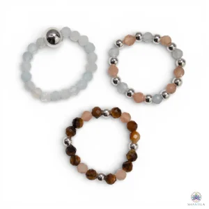 Trio de bagues élastiques en pierres naturelles — aigue-marine, pierre de soleil et œil de tigre — présentées sur fond neutre avec perles argentées, dans une palette de bleu côtier, or chaud et brun doré.