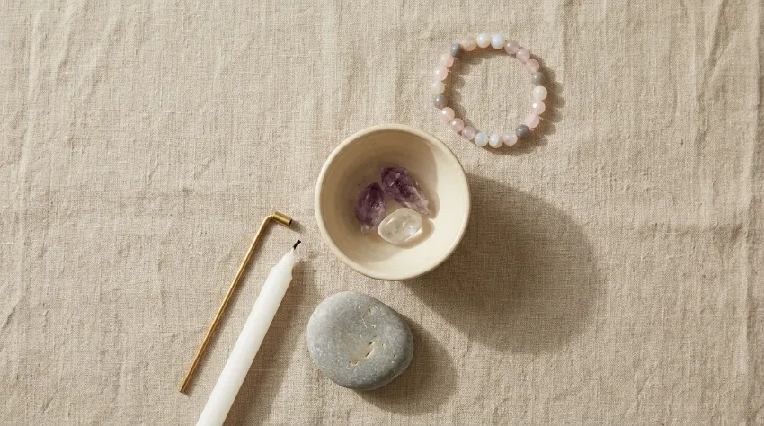 Pierres et astrologie : choisir sa pierre selon son signe astrologique 4 Bracelet de pierres, galet et bol en céramique sur lin beige — scène de rituel quotidien pour illustrer comment utiliser ses pierres au quotidien